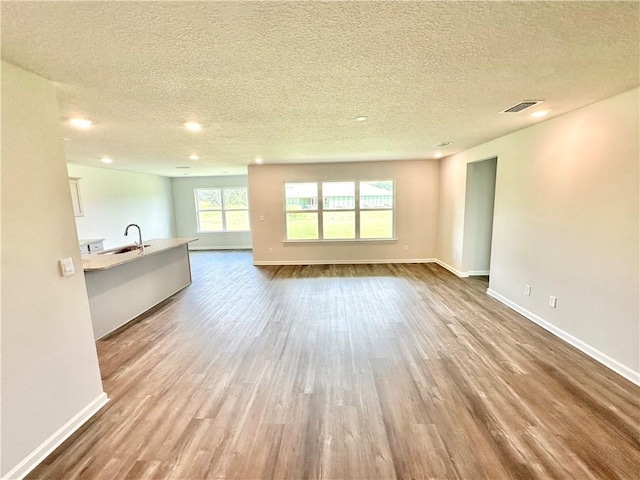 unfurnished living room featuring a textured ceiling, light hardwood / wood-style floors, and sink