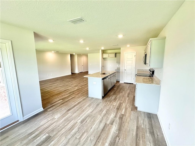 kitchen with sink, an island with sink, light hardwood / wood-style floors, a textured ceiling, and appliances with stainless steel finishes