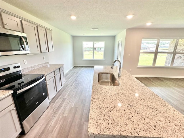 kitchen featuring a textured ceiling, light stone counters, sink, and stainless steel appliances