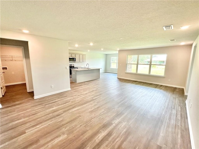 unfurnished living room with a textured ceiling, light wood-type flooring, and sink