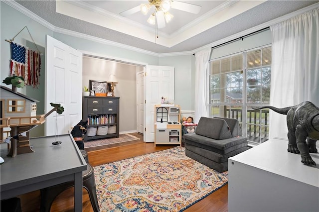 office area with a tray ceiling, wood finished floors, a ceiling fan, and crown molding