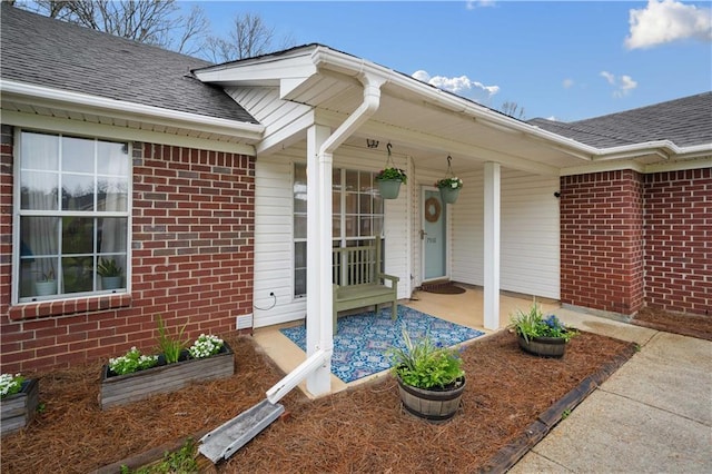 doorway to property with a porch, brick siding, and roof with shingles