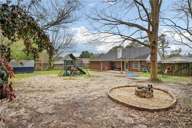 view of yard with an outdoor fire pit, a fenced backyard, and a playground