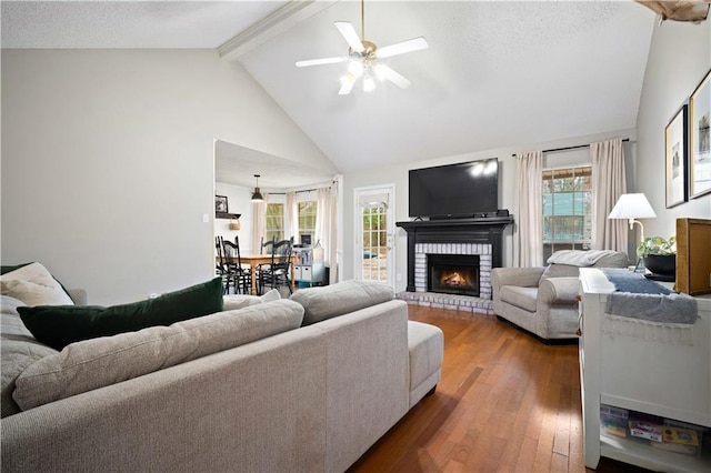 living area with a brick fireplace, beam ceiling, high vaulted ceiling, a ceiling fan, and wood-type flooring