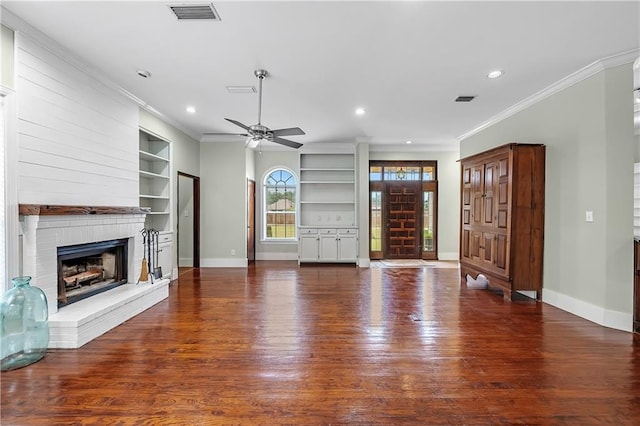 unfurnished living room with ceiling fan, built in features, ornamental molding, wood-type flooring, and a fireplace