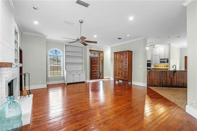 unfurnished living room featuring ceiling fan, built in shelves, wood-type flooring, sink, and a fireplace