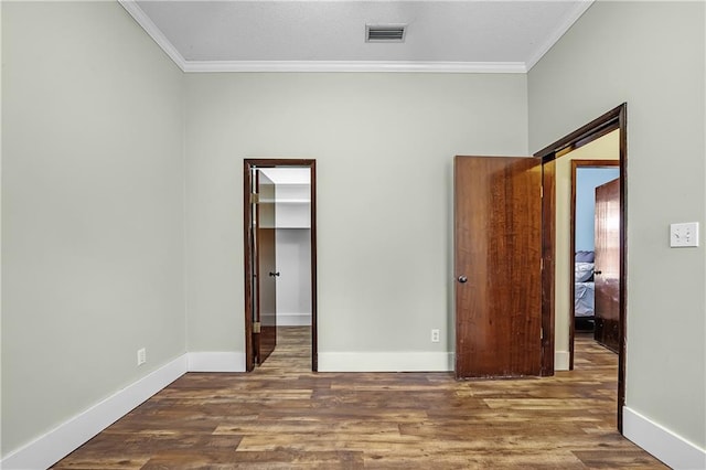 unfurnished bedroom featuring a closet, a spacious closet, crown molding, and hardwood / wood-style floors