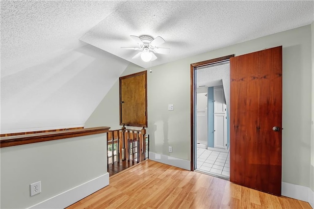 unfurnished room featuring a textured ceiling, light hardwood / wood-style flooring, ceiling fan, and lofted ceiling