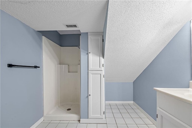 bathroom featuring tile patterned flooring, a textured ceiling, vanity, and walk in shower