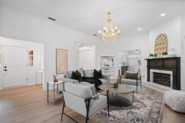 living room featuring a stone fireplace, crown molding, built in features, and light wood-type flooring