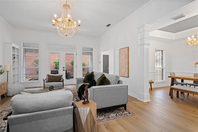 living room with decorative columns, french doors, ornamental molding, light hardwood / wood-style floors, and a chandelier