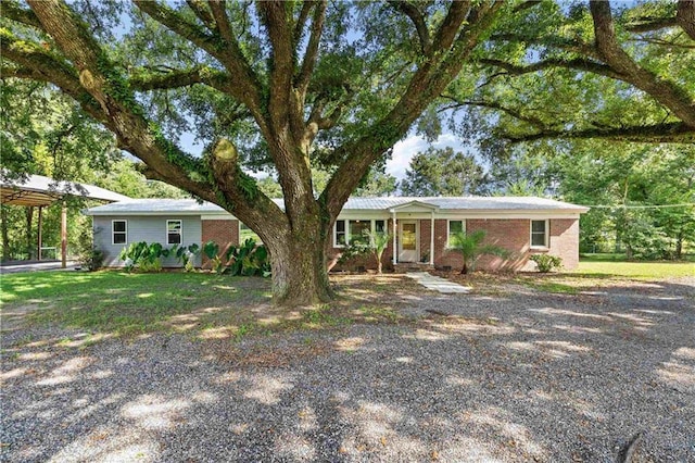 ranch-style home featuring brick siding, gravel driveway, and a detached carport