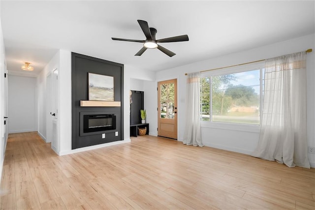 unfurnished living room with ceiling fan, a large fireplace, and light wood-type flooring