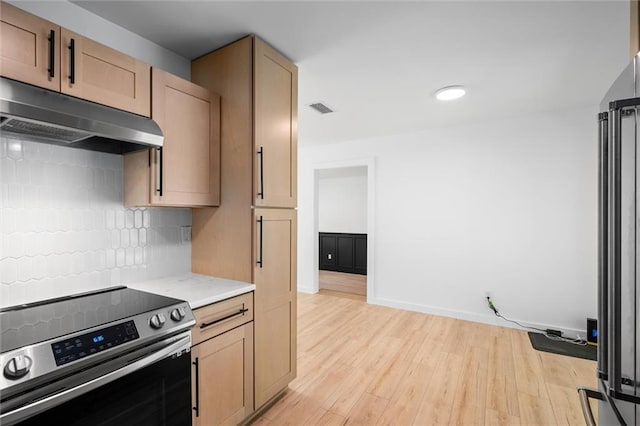 kitchen with stainless steel electric stove, decorative backsplash, light brown cabinets, and light wood-type flooring