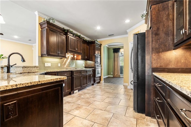 kitchen with black fridge, backsplash, dark brown cabinets, stainless steel oven, and sink