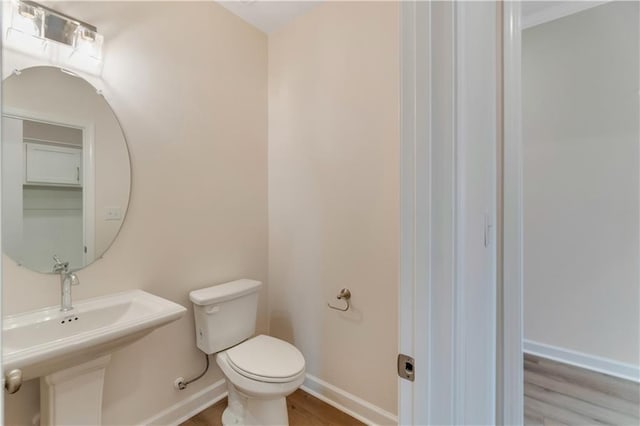half bathroom featuring toilet, baseboards, and wood finished floors