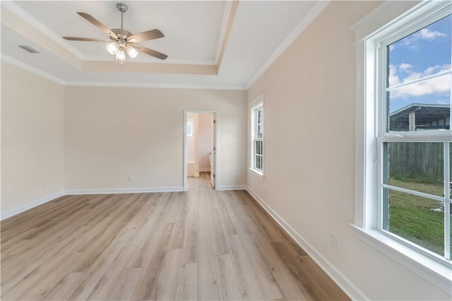 empty room with crown molding, light wood finished floors, a ceiling fan, a tray ceiling, and visible vents