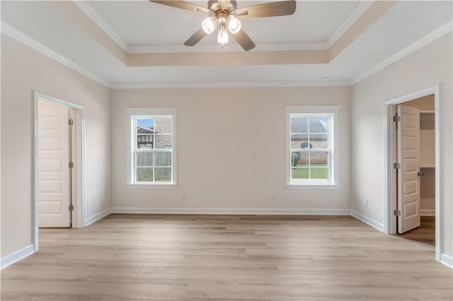 unfurnished bedroom featuring crown molding, a tray ceiling, baseboards, and light wood-style flooring