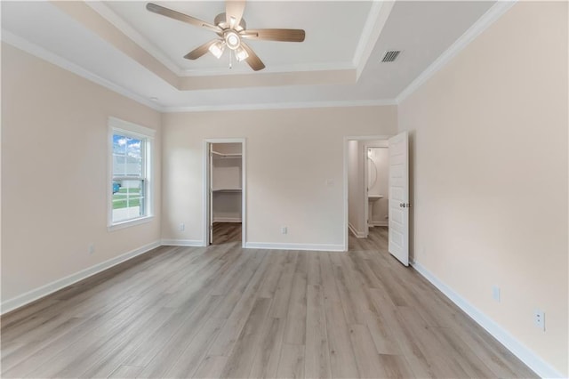 unfurnished bedroom featuring light wood-style flooring, a spacious closet, a tray ceiling, visible vents, and a closet