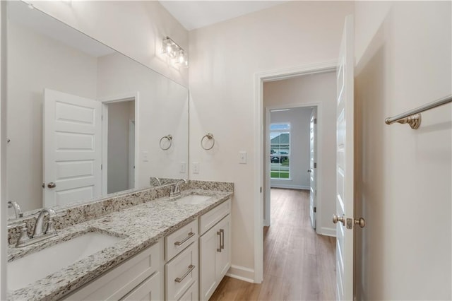 bathroom with a sink, baseboards, double vanity, and wood finished floors