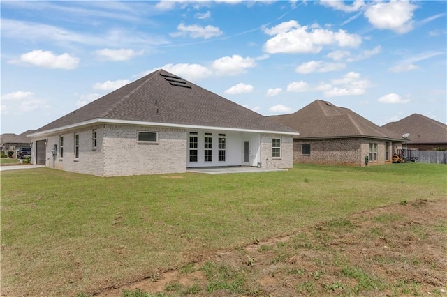 back of property with a lawn, an attached garage, french doors, and brick siding