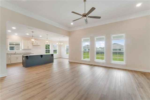 unfurnished living room featuring light wood-style flooring, ceiling fan with notable chandelier, recessed lighting, baseboards, and ornamental molding