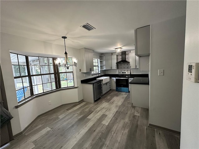 kitchen featuring an inviting chandelier, appliances with stainless steel finishes, sink, wall chimney range hood, and light wood-type flooring