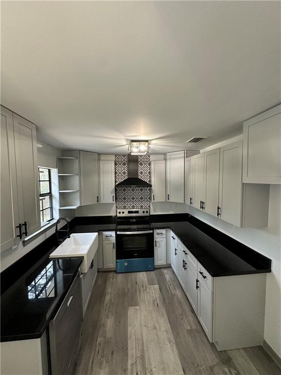 kitchen featuring wall chimney exhaust hood, backsplash, sink, light wood-type flooring, and stainless steel range with electric cooktop