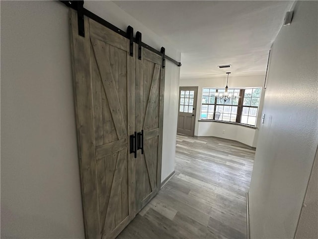 hallway with a chandelier, a barn door, and light hardwood / wood-style floors