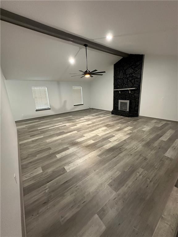 unfurnished living room featuring hardwood / wood-style floors, ceiling fan, lofted ceiling with beams, and a stone fireplace