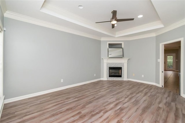 unfurnished living room with a tiled fireplace, crown molding, a raised ceiling, and light wood-type flooring