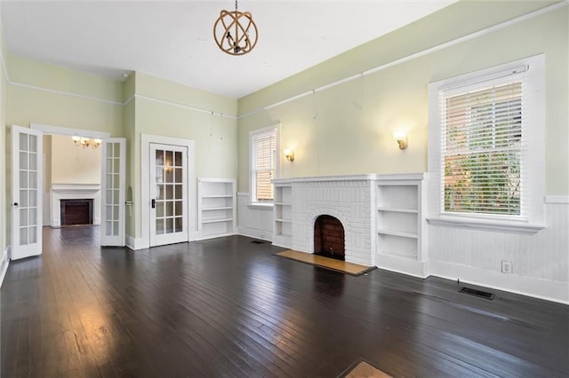 unfurnished living room with an inviting chandelier, dark hardwood / wood-style flooring, a fireplace, and french doors