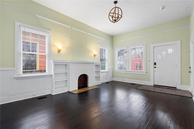 unfurnished living room with an inviting chandelier, a brick fireplace, and hardwood / wood-style flooring