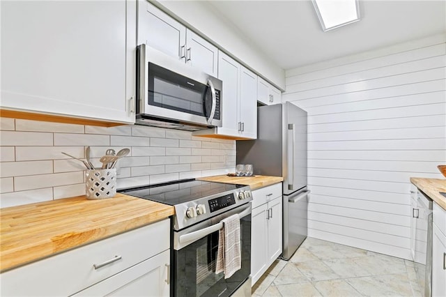 kitchen with light tile patterned floors, backsplash, white cabinetry, appliances with stainless steel finishes, and butcher block counters