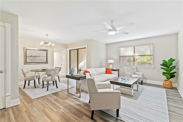 living room featuring ceiling fan with notable chandelier and light hardwood / wood-style flooring