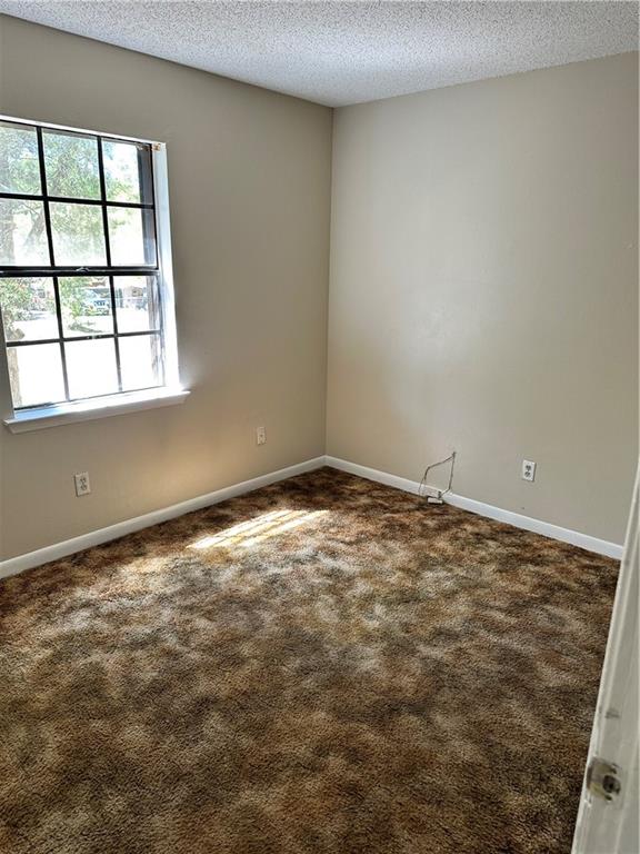 unfurnished room with a textured ceiling and dark carpet