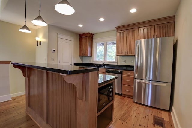 kitchen featuring light wood-type flooring, stainless steel appliances, pendant lighting, a kitchen island, and a breakfast bar area