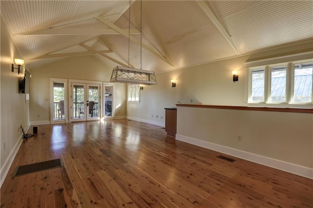 unfurnished living room featuring french doors, hardwood / wood-style floors, vaulted ceiling with beams, and a wealth of natural light