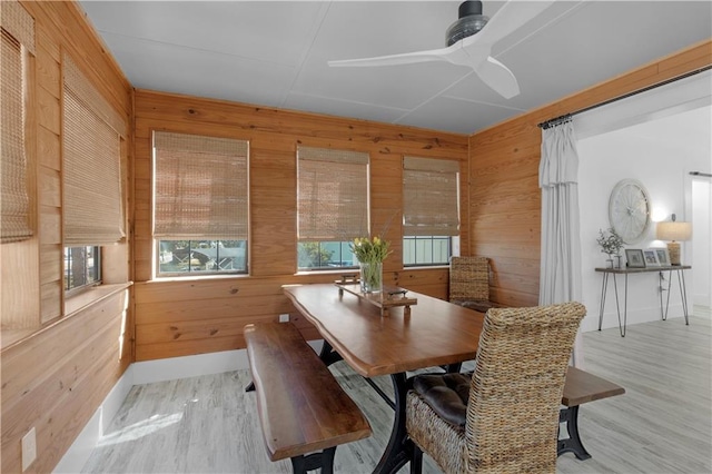 dining room featuring baseboards, wood walls, ceiling fan, and wood finished floors