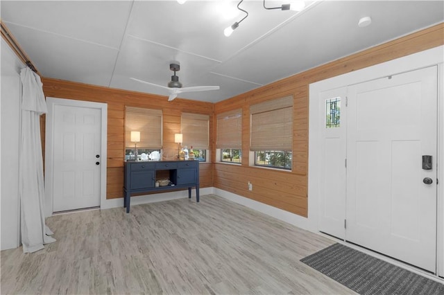 entrance foyer featuring a ceiling fan, a healthy amount of sunlight, wood walls, and wood finished floors