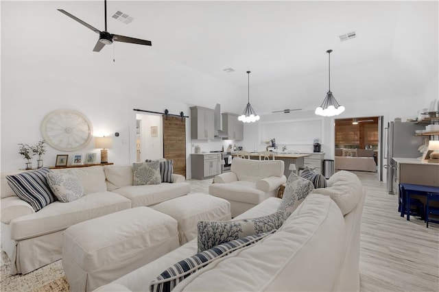 living room with high vaulted ceiling, a barn door, visible vents, and ceiling fan with notable chandelier