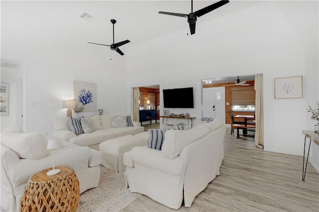 living area featuring a towering ceiling, light wood-type flooring, visible vents, and a ceiling fan