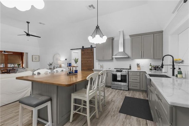 kitchen with gray cabinets, stainless steel range with gas stovetop, visible vents, wall chimney exhaust hood, and ceiling fan