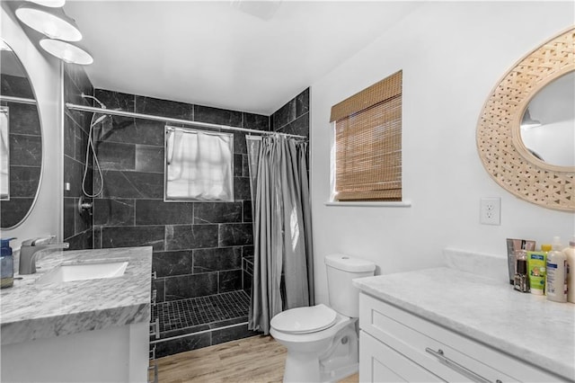 full bathroom with vanity, toilet, wood finished floors, and tiled shower