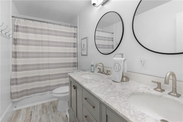 full bath with double vanity, toilet, wood finished floors, and a sink