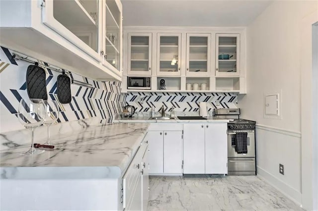 kitchen featuring white cabinets, light stone countertops, backsplash, and stainless steel stove