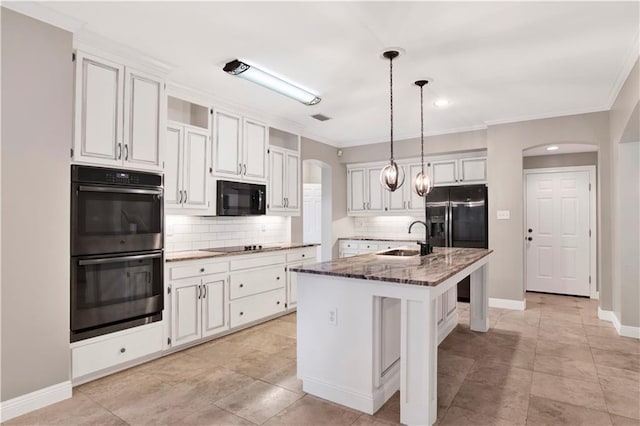 kitchen with sink, dark stone counters, a center island with sink, white cabinets, and black appliances