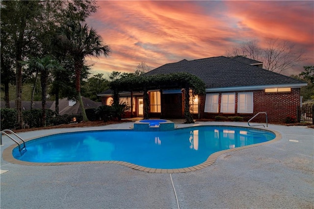 pool at dusk featuring an in ground hot tub and a patio area