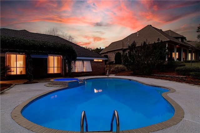 pool at dusk with an in ground hot tub and a patio