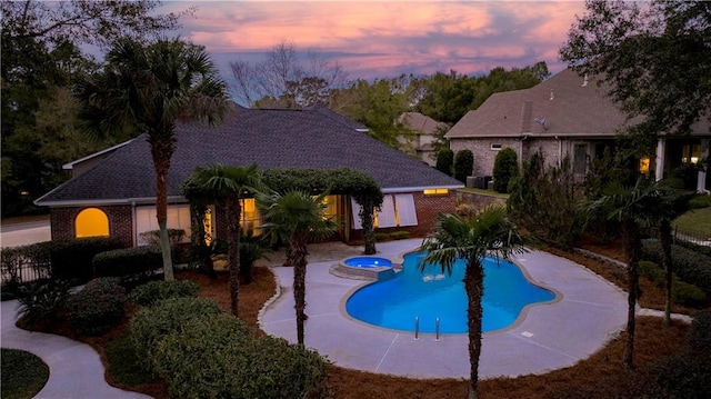 pool at dusk featuring an in ground hot tub and a patio area